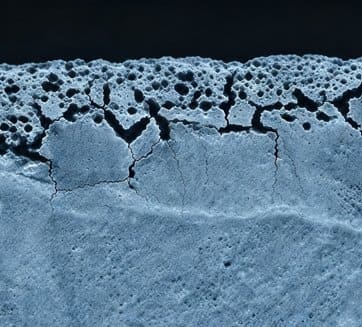 Micrograph cross-section of steel strip showing a porous band of alloying element oxides formed just below the surface rather than on it