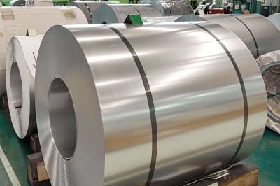 Strapped stainless steel coil resting on a timber cradle in a steel warehouse