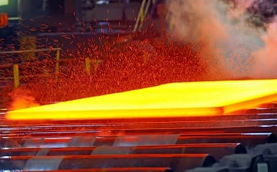 Hot steel rolling mill production showing capital-intensive manufacturing with glowing molten steel and industrial equipment